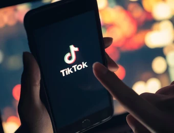 Nahaufnahme eines Smartphones mit dem TikTok-Logo auf dem Bildschirm; unscharfer, bunter Hintergrund.