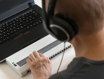 Person mit Kopfhörern vor Laptop, bedient einen weißen Controller mit vielen kleinen Tasten.