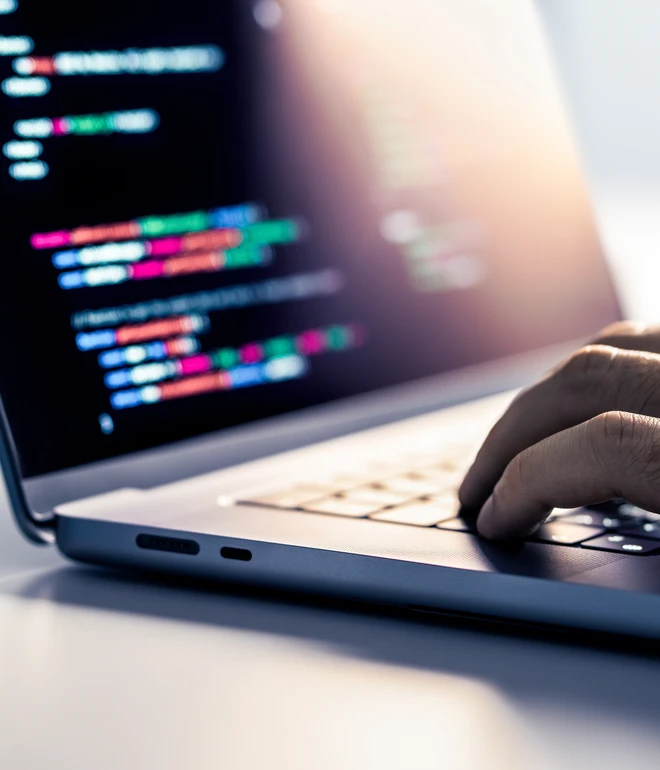 Nahaufnahme eines Laptops mit farbigem Code im Display; eine Hand tippt auf der Tastatur.