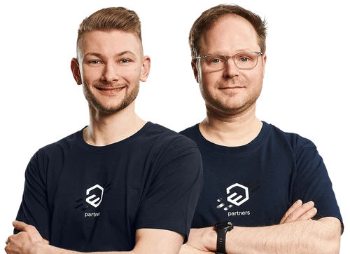 Zwei Männer stehen nebeneinander, tragen dunkelblaue T-Shirts mit Logo; beide verschränken die Arme.