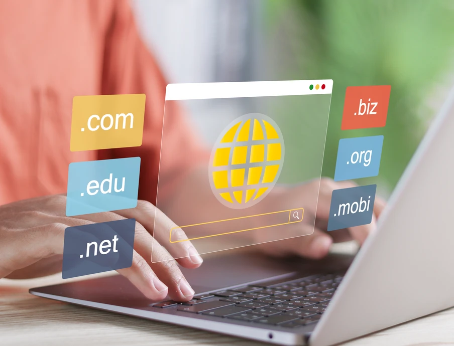 Person tippt auf Laptop; schwebende bunte Domain-Labels (.com,.net,.org,.edu,.biz,.mobi) und Globus-Symbol.